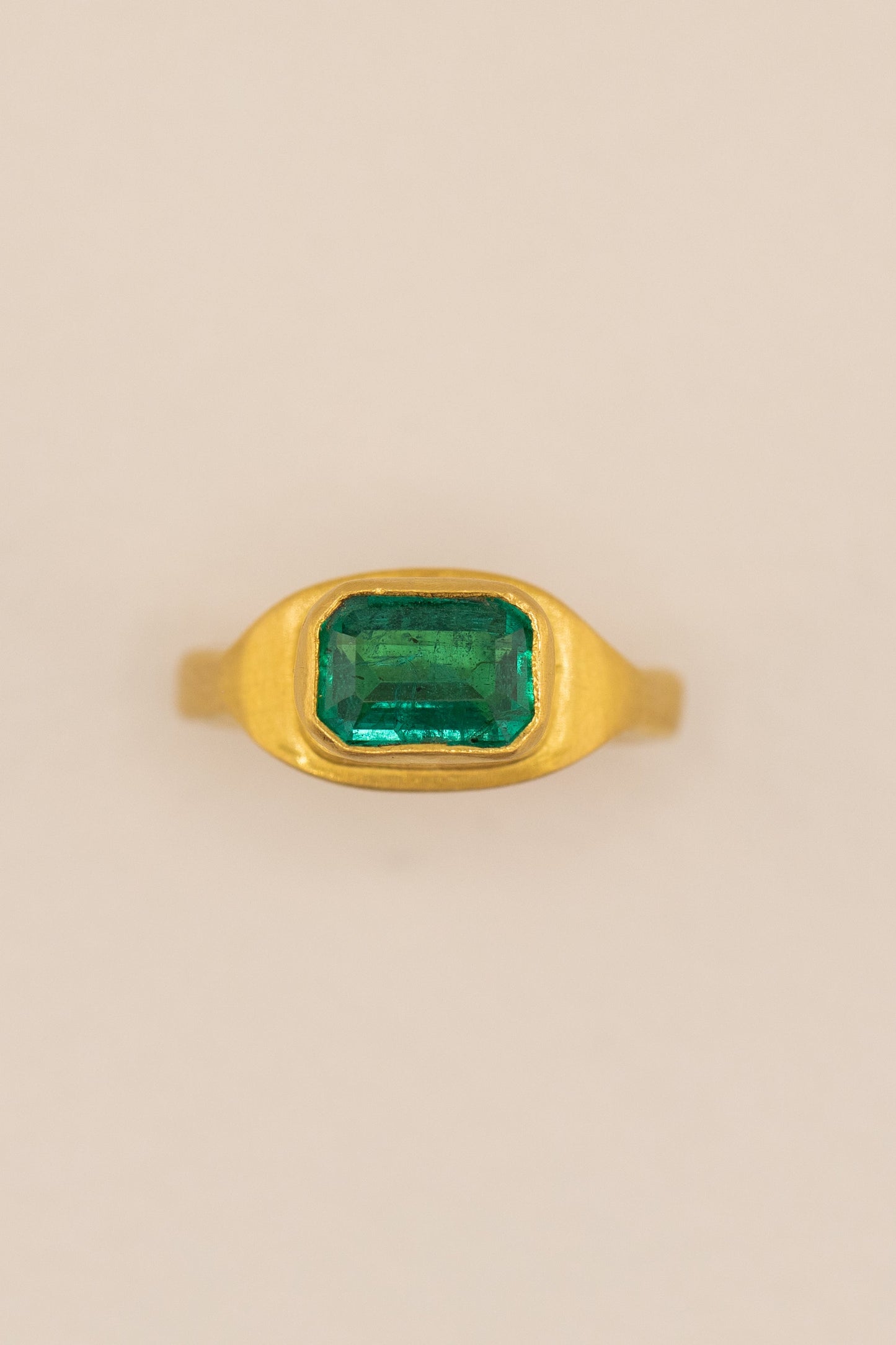 Gold ring with a green gemstone on a beige background