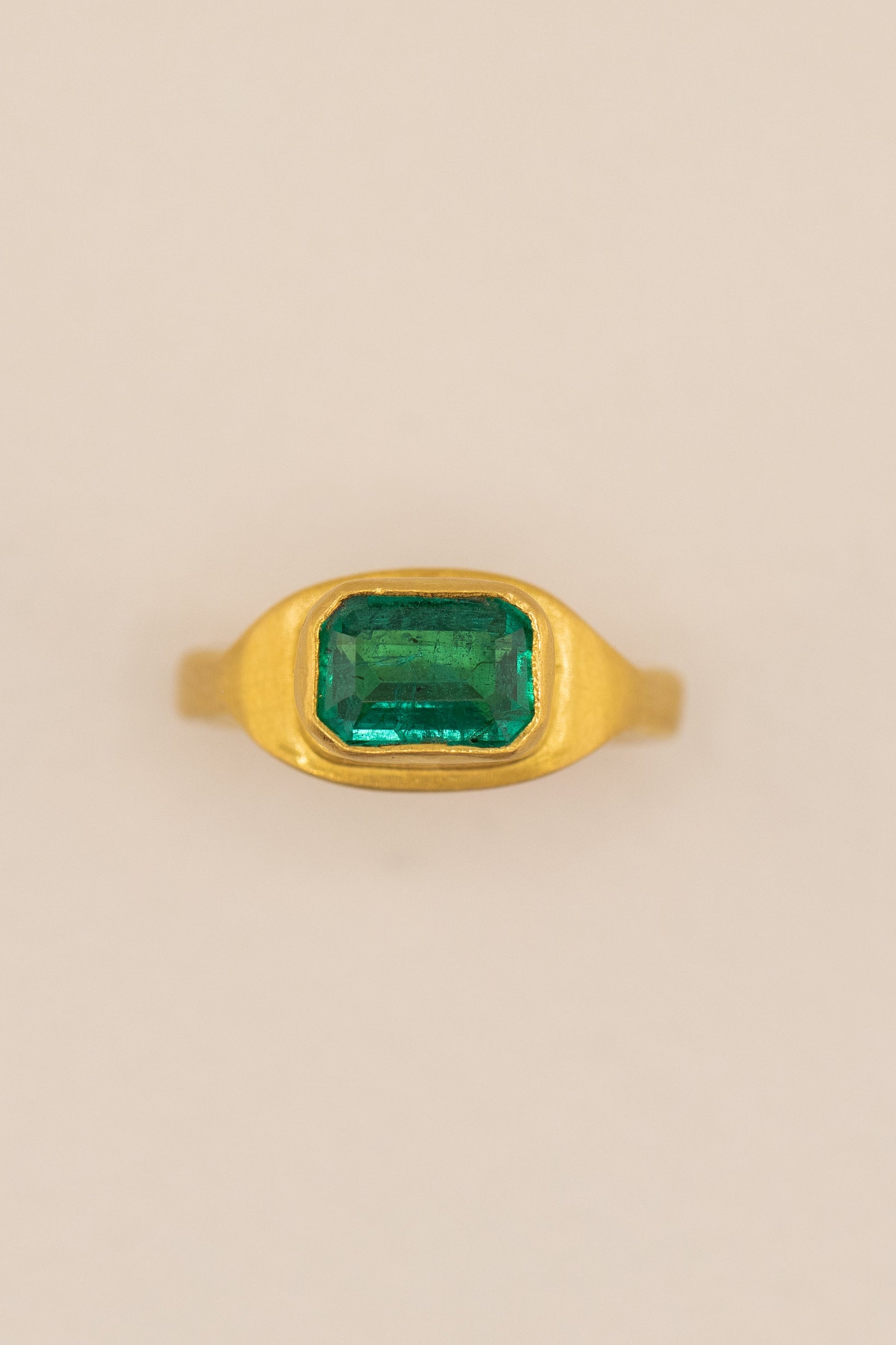 Gold ring with a green gemstone on a beige background