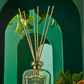 Reed diffuser with decorative sticks in a green bottle against a green arch background