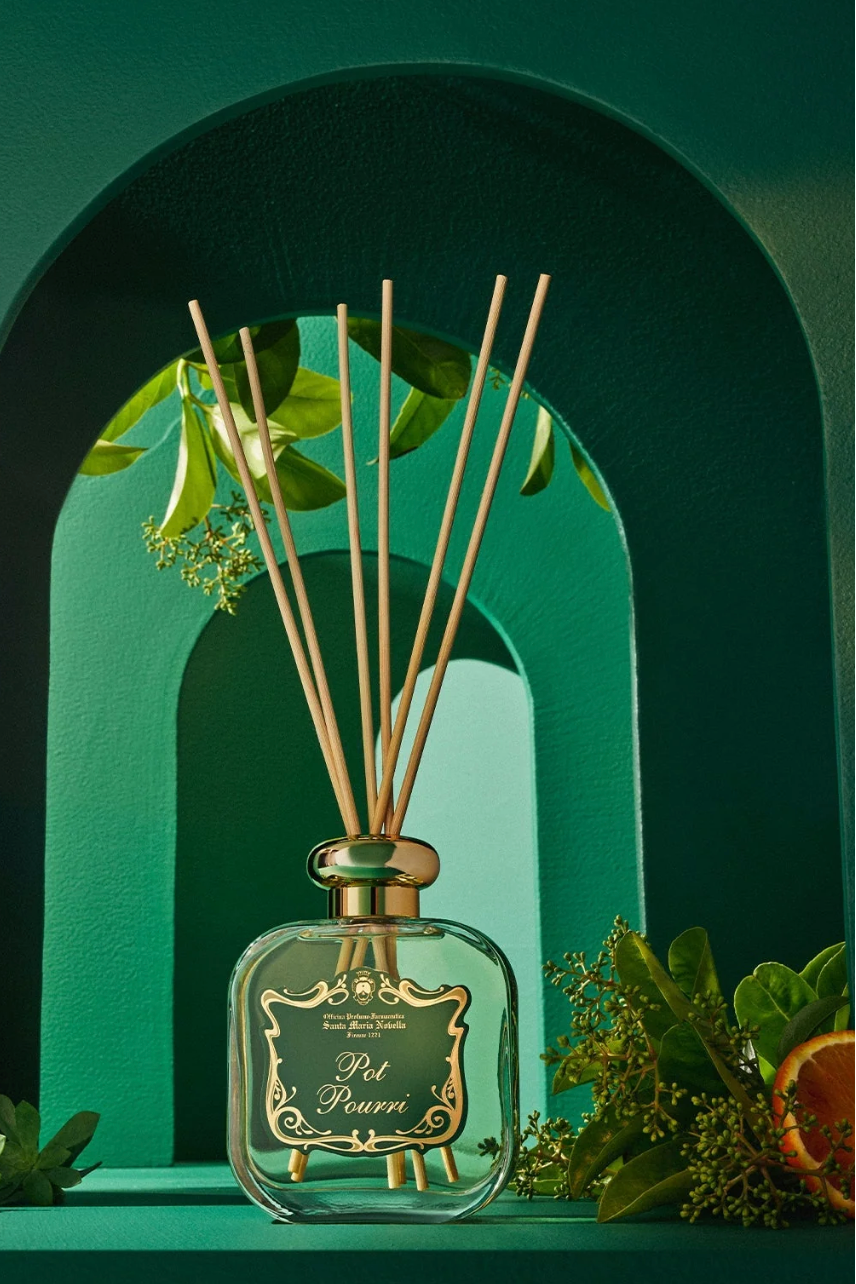 Reed diffuser with decorative sticks in a green bottle against a green arch background