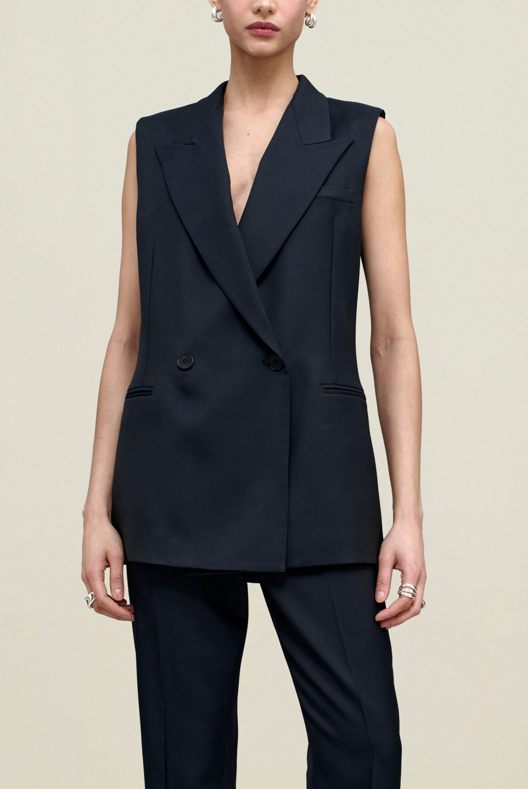 Person wearing a black sleeveless blazer and pants on a beige background