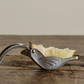 Metallic bird-shaped butter knife with a small piece of butter on a wooden surface