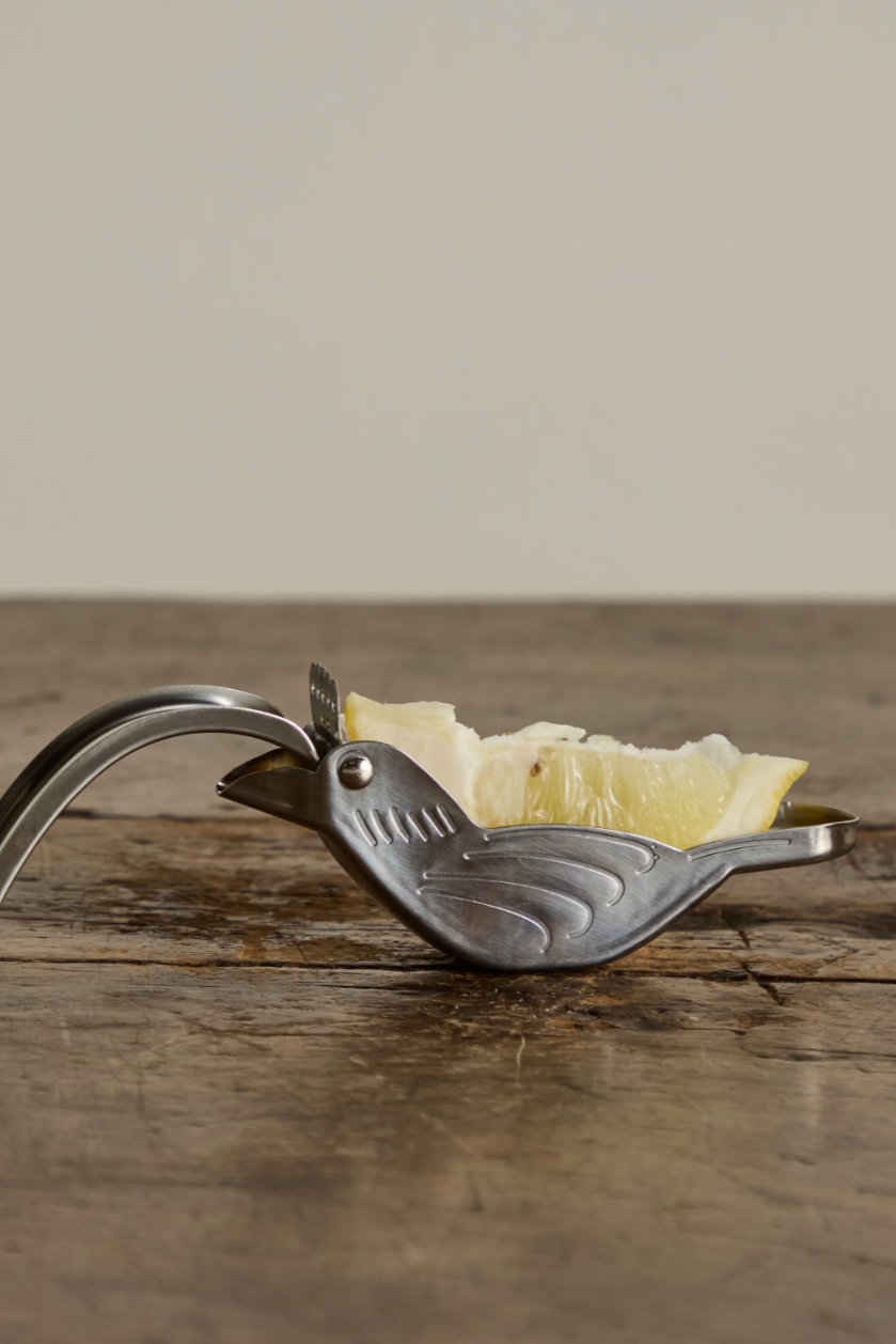 Metallic bird-shaped butter knife with a small piece of butter on a wooden surface