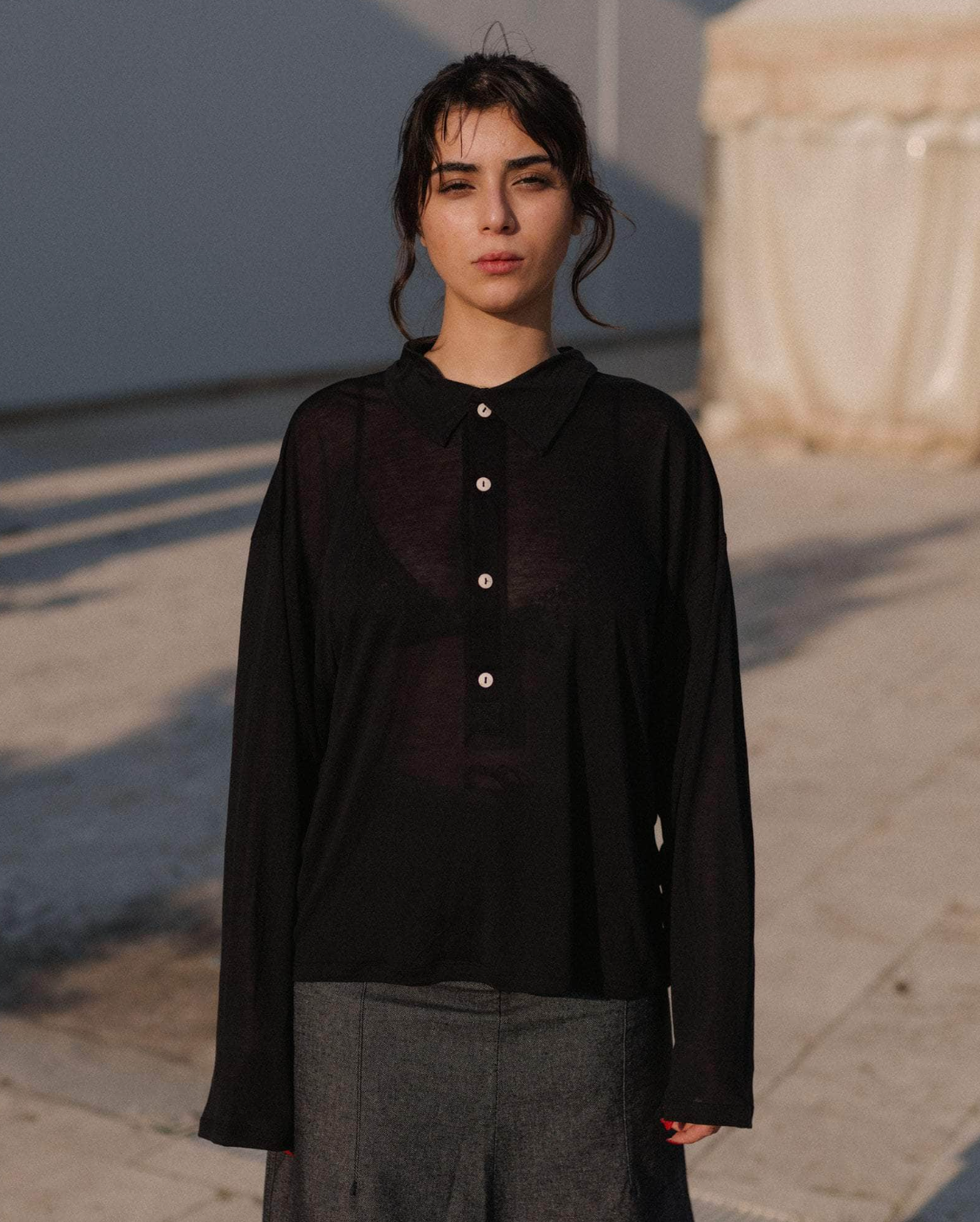 Woman wearing a black shirt and gray pants standing outdoors.