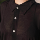 Close-up of a person wearing a dark brown button-up shirt with a blurred background