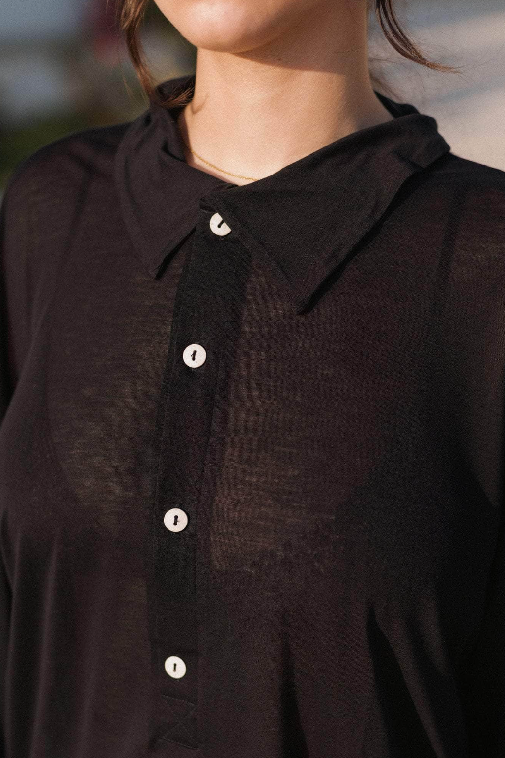 Close-up of a person wearing a dark brown button-up shirt with a blurred background