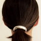 Person with a ponytail held by a silver hair tie against a neutral background
