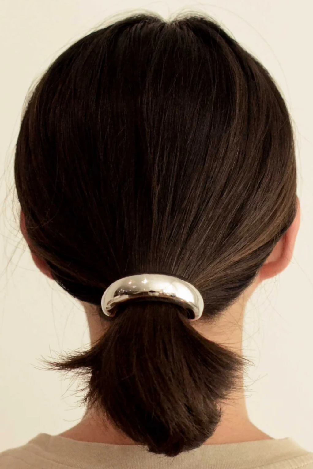 Person with a ponytail held by a silver hair tie against a neutral background