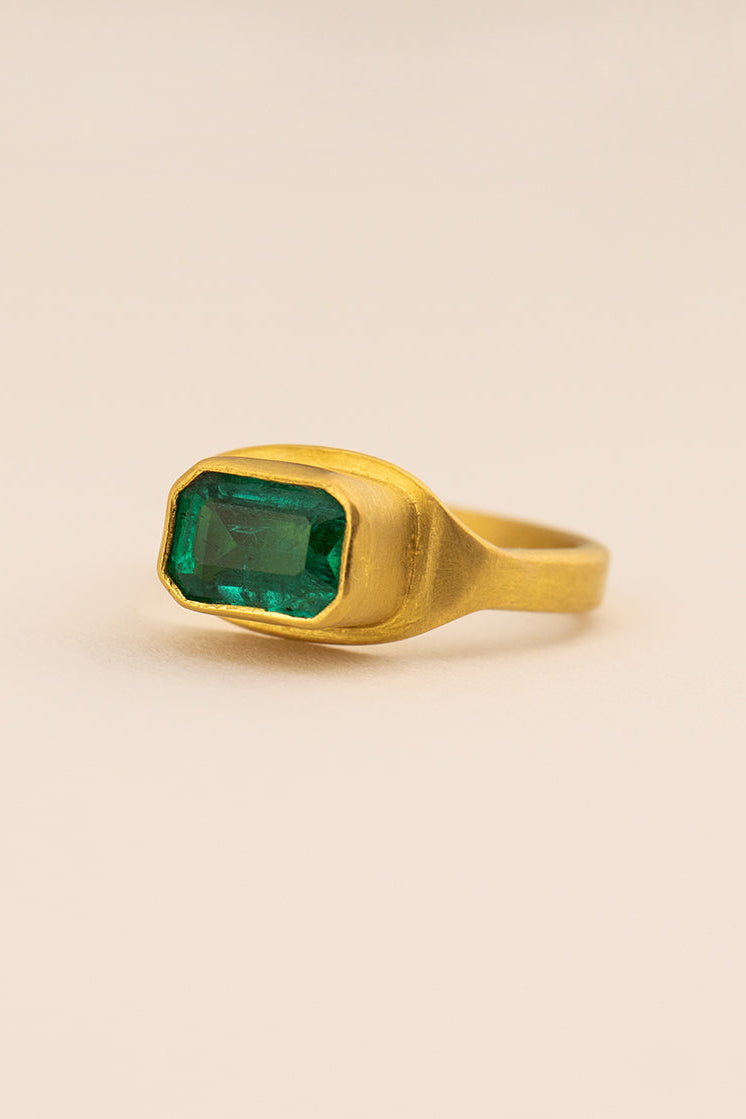 Gold ring with a green gemstone on a beige background